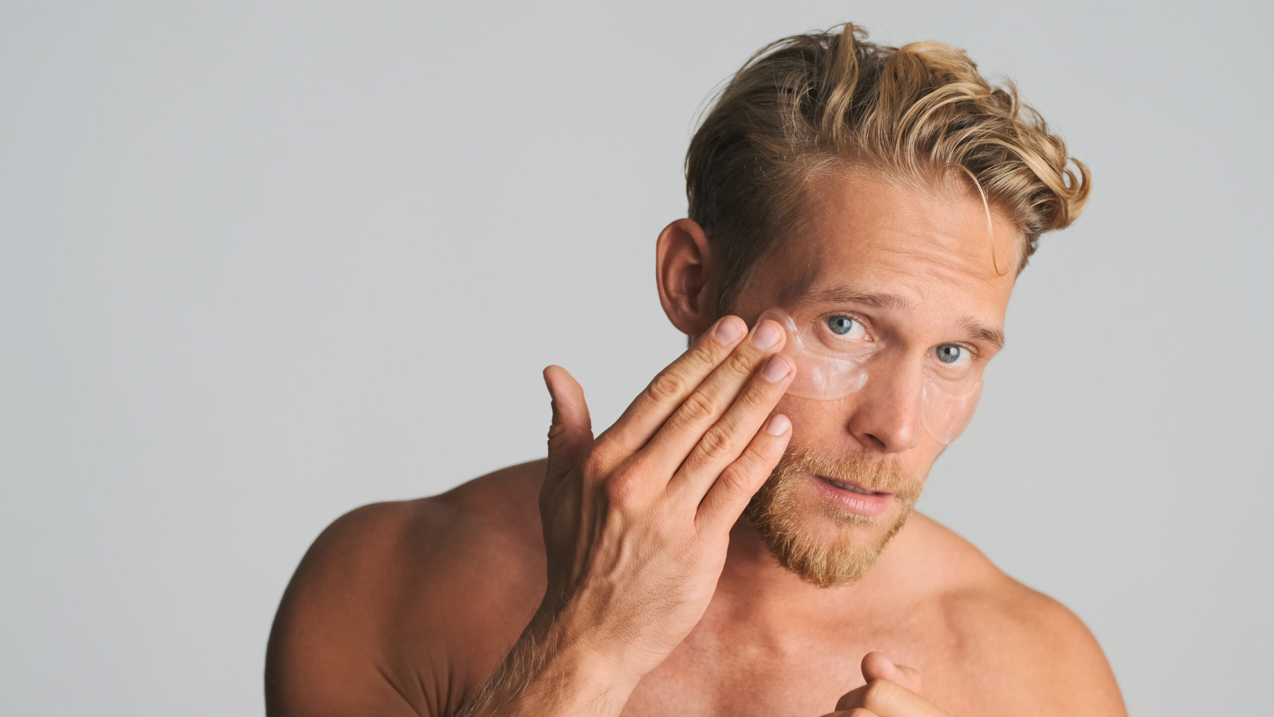 Handsome bearded man applying eye patches take care of his skin